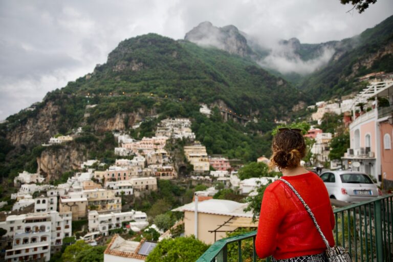 mujer con chaqueta roja de pie en la cima de un edificio mirando a la montaña verde durante el día